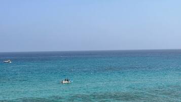 A coastal scene with clear turquoise waters, a few boats, and people swimming.