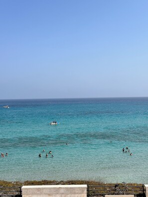 A coastal scene with clear turquoise waters, a few boats, and people swimming.