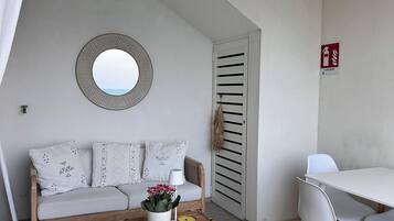 Quarto com sofá branco, espelho redondo, mesa de madeira com planta em vaso e cadeira branca.