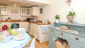 Une cuisine avec des meubles blancs, un plan de travail en bois, un évier et un coin repas avec une table mise pour deux personnes.