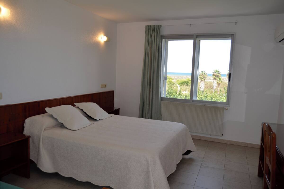 Ein Schlafzimmer mit Bett, Nachttisch, Fenster mit Meerblick und Heizkörper.