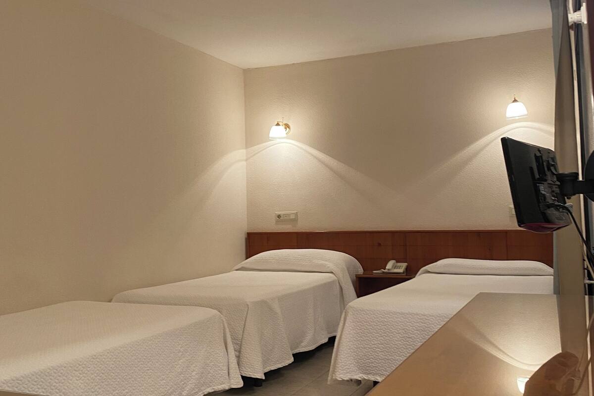 Ein Hotelzimmer mit zwei Einzelbetten, einem Holztisch und zwei Wandleuchten.
