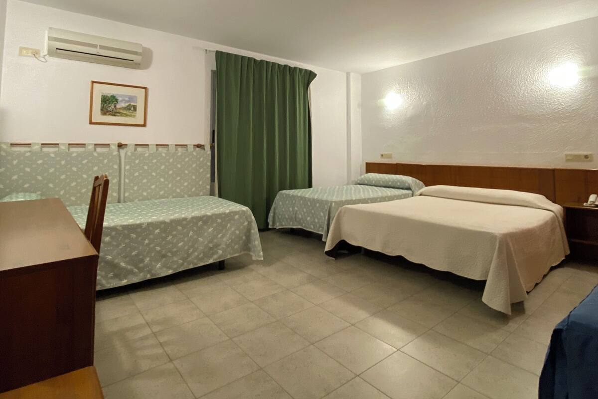 Ein Hotelzimmer mit zwei Einzelbetten, einem Holztisch, einem grünen Vorhang und einer Klimaanlage an der Wand.
