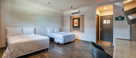 Habitación de hotel con dos camas, un escritorio y una silla. Se observa un cuadro en la pared y un equipo de aire acondicionado sobre la cama.