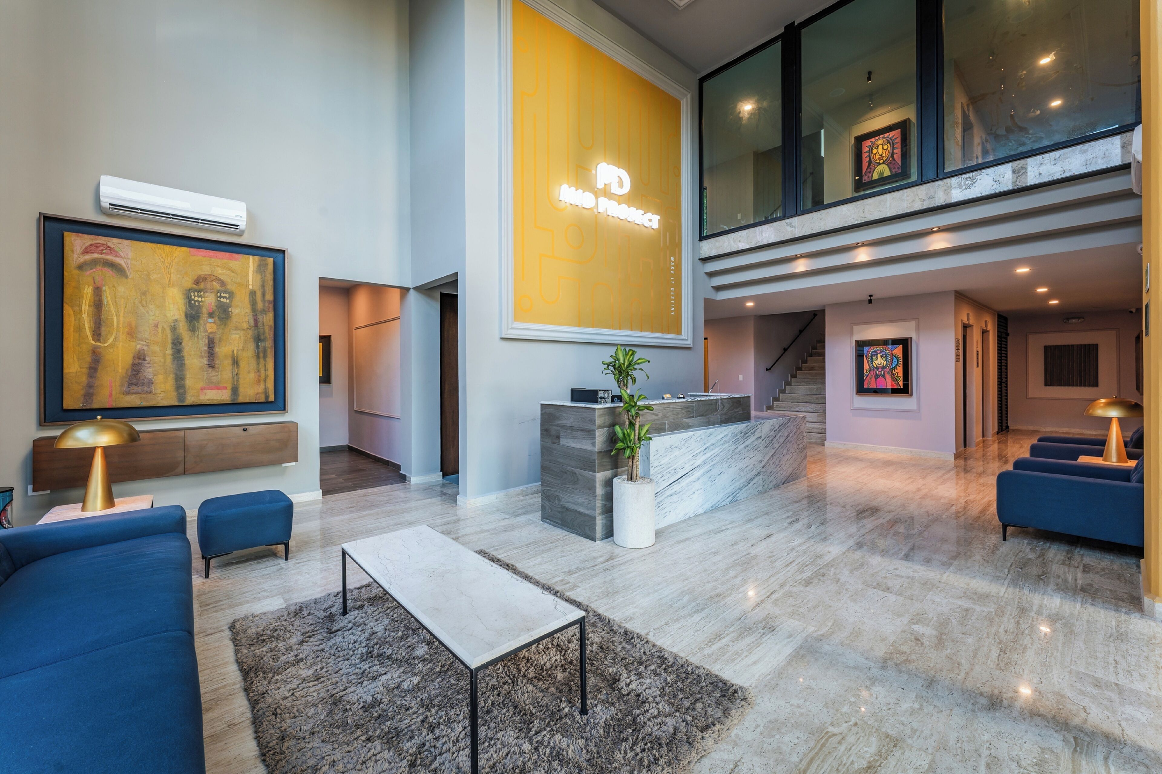 A spacious living area with a modern design, featuring a large sofa, a coffee table, and a reception desk with a potted plant.