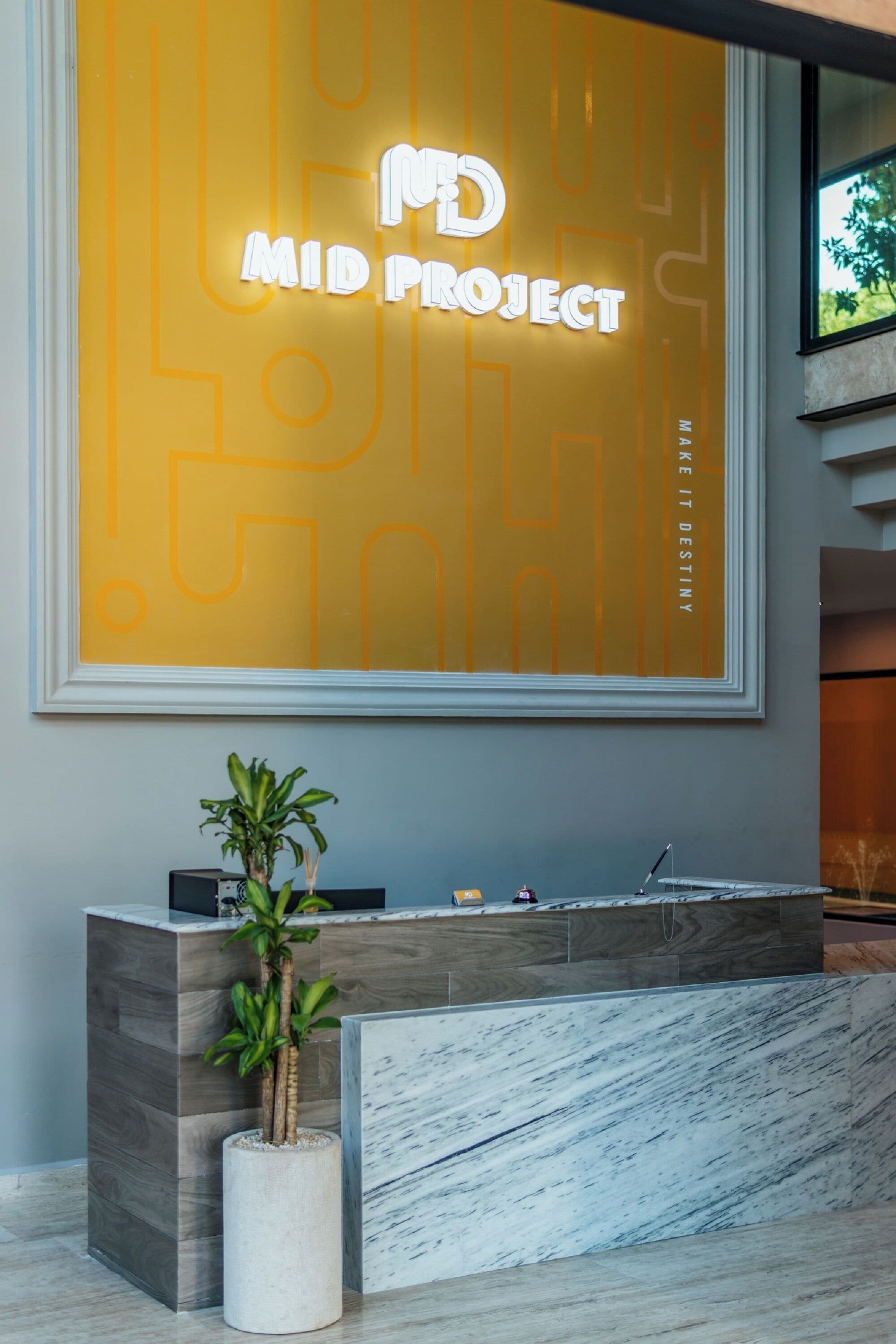 A reception desk with a modern design, a large illuminated sign above it, and a potted plant beside the desk.