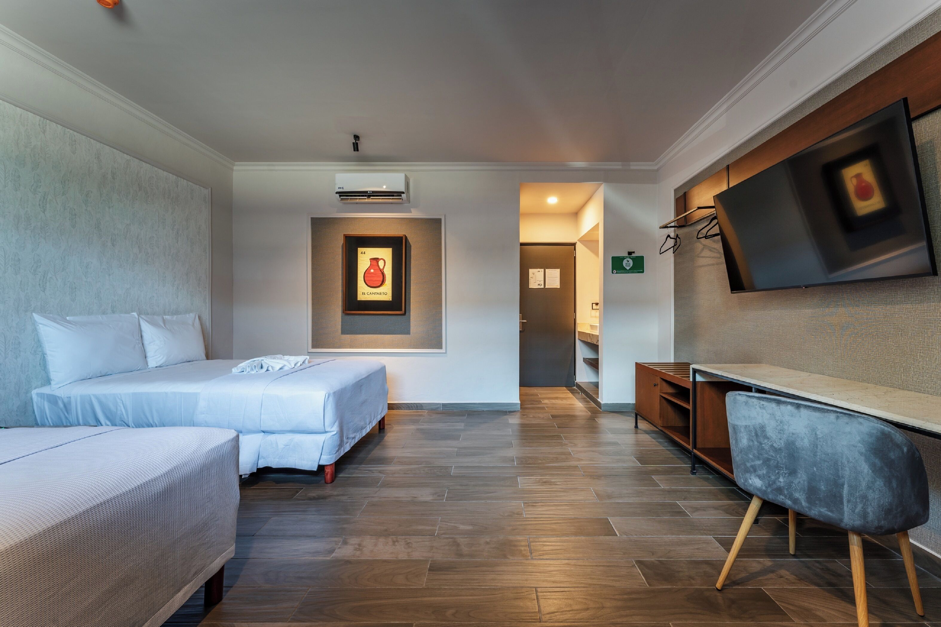 A hotel room with two beds, a desk, a TV, and a framed picture on the wall.