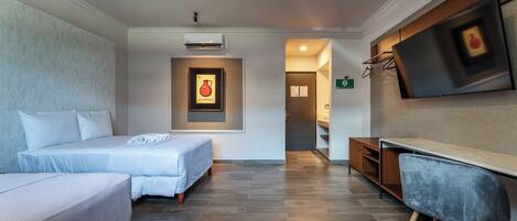 A hotel room with two beds, a desk, a TV, and a framed picture on the wall.