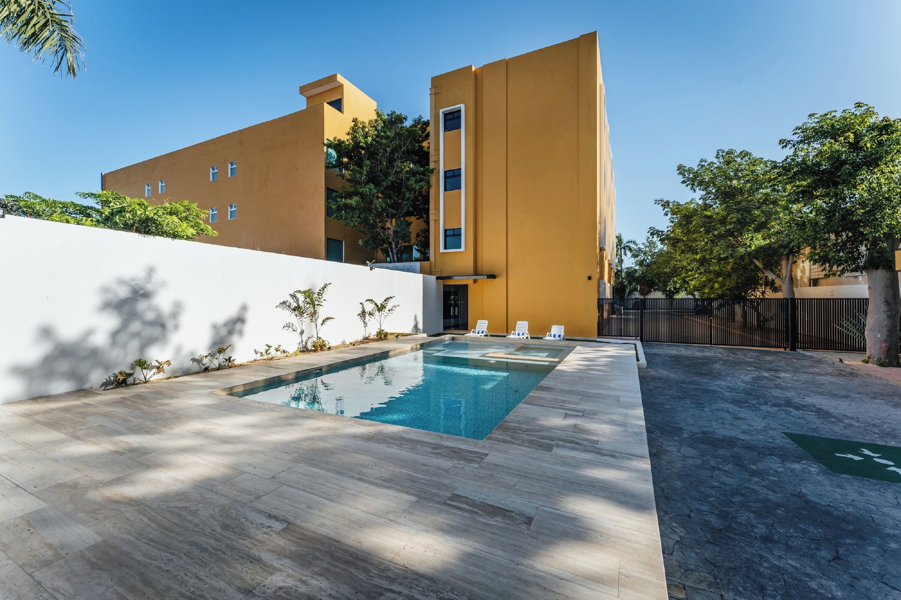 A modern building with a swimming pool, outdoor seating, and a clear sky.