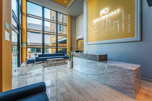 A modern lobby with a reception desk, seating area, and large windows.