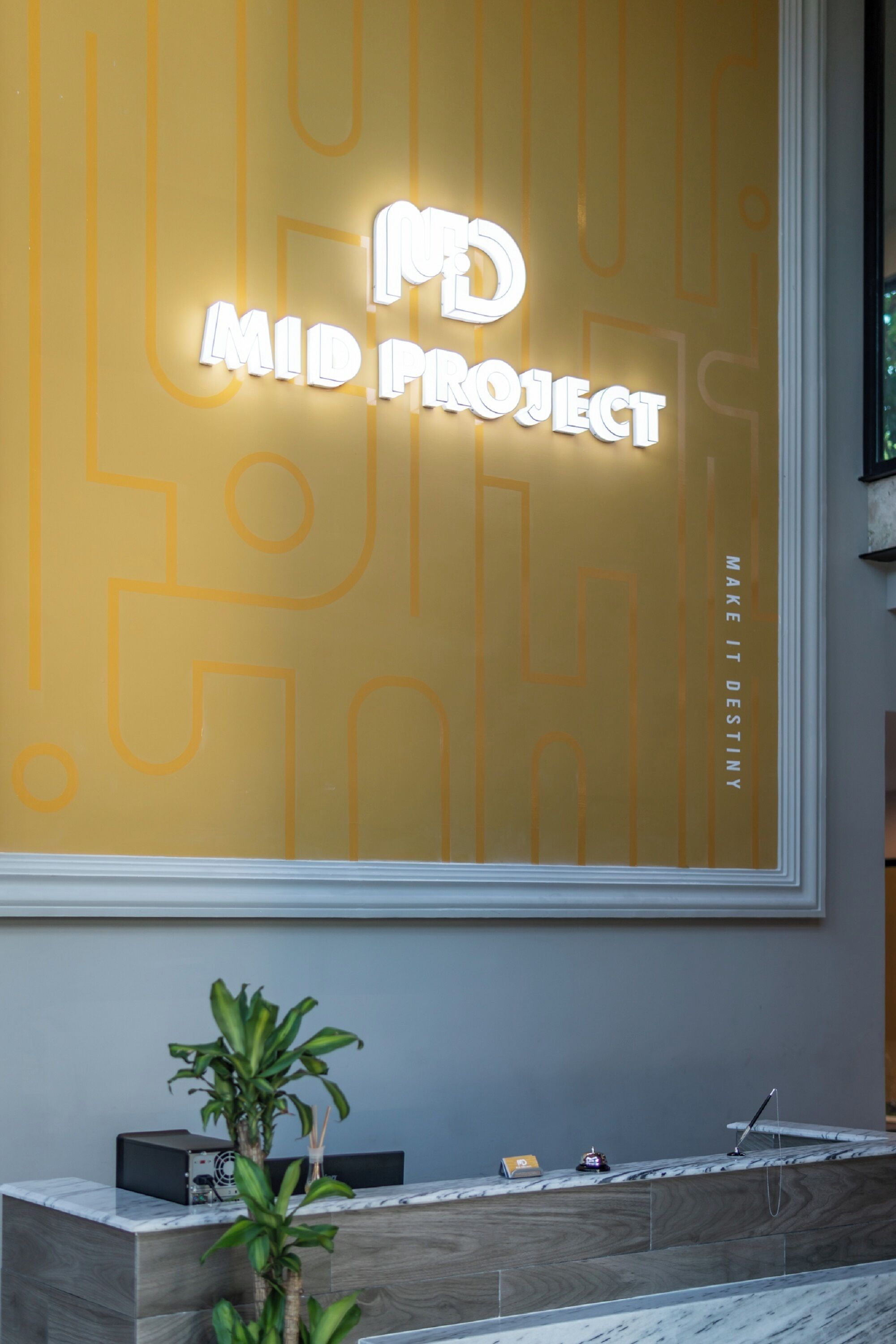 Una reception dal design moderno, una pianta in vaso e un cartello con la scritta 'Mid Project'.