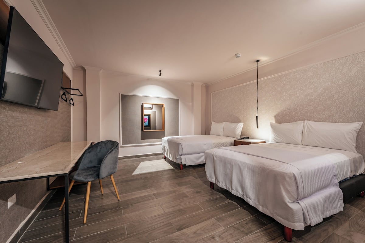 A hotel room with two beds, a desk, a chair, and a TV.