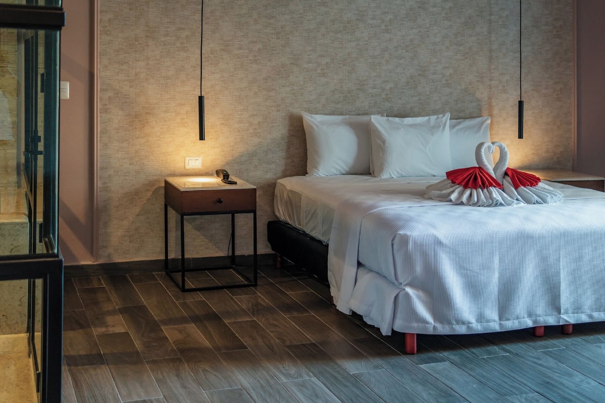 A hotel room with a bed, bedside table, and a wall-mounted light fixture.