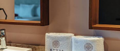 A bathroom with a marble countertop, two sinks, and a mirror. There are towels and toiletries on the counter.
