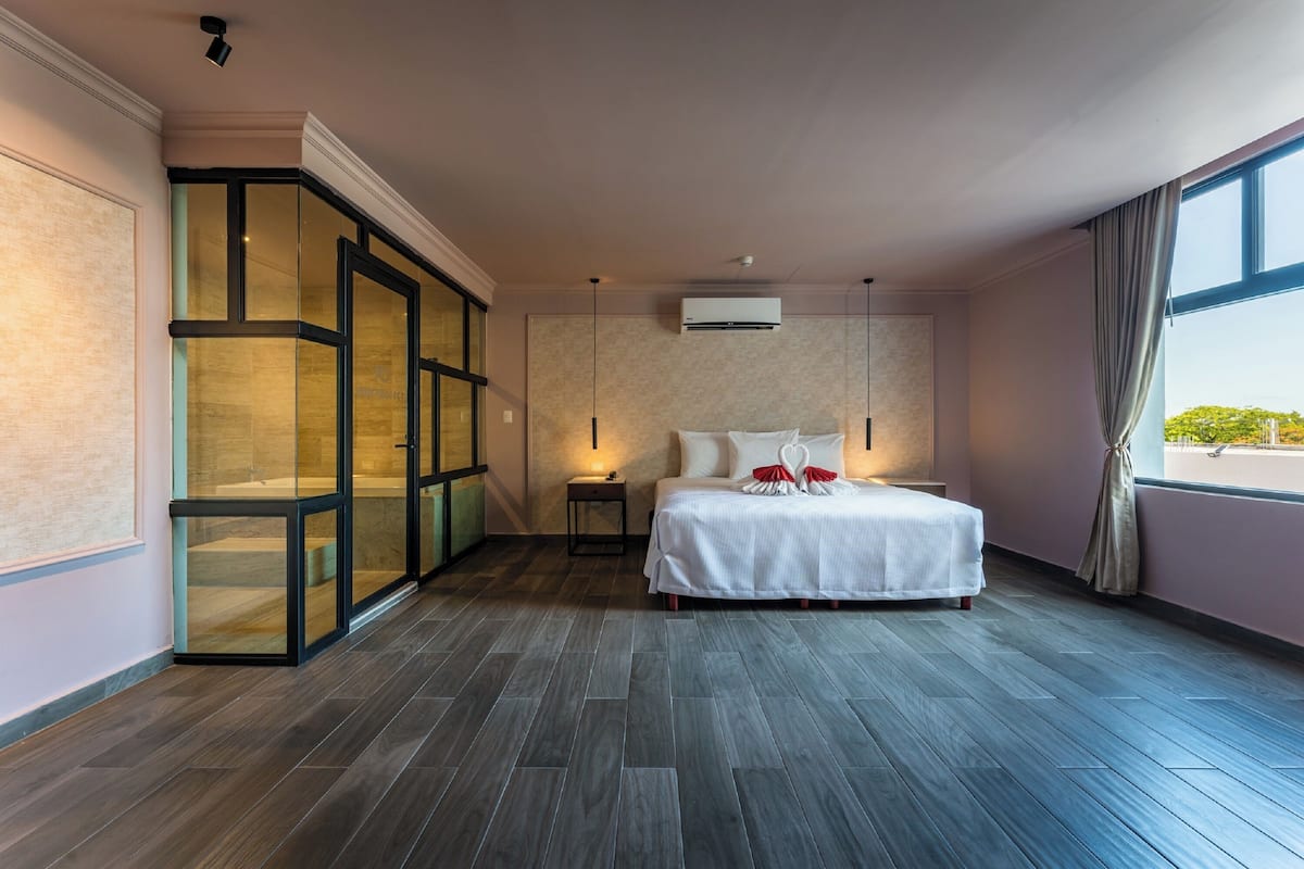 A bedroom with a large bed, a glass partition, a nightstand, and a window with curtains.