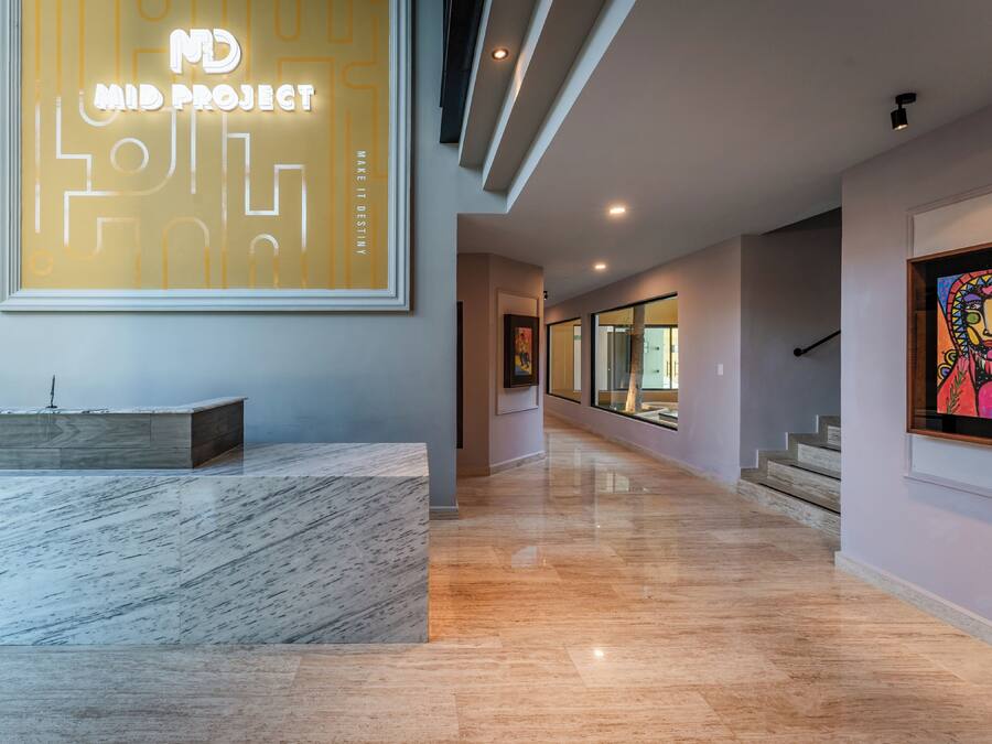 A modern lobby with a marble reception desk, a large illuminated sign, and a staircase leading to upper floors.