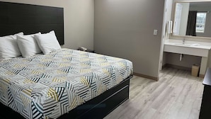A bedroom with a bed, bedside table, and a bathroom with a sink and mirror. - Studio 6 Suites West Memphis, AR - Memphis (West Memphis)