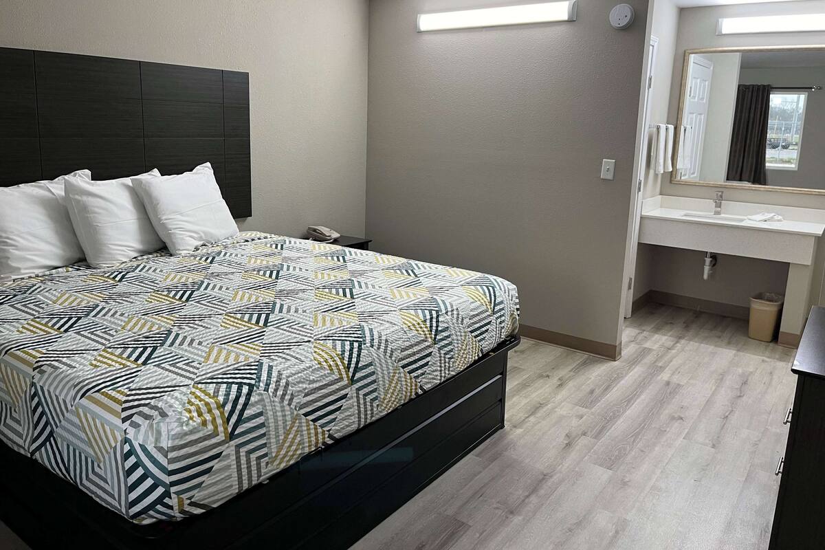 Ein Schlafzimmer mit Bett, Nachttisch und einem Badezimmer mit Waschbecken und Spiegel.