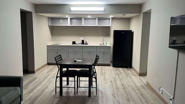 A compact kitchen with grey cabinets, a black refrigerator, and a dining table with chairs. - Studio 6 Suites West Memphis, AR - Memphis (West Memphis)