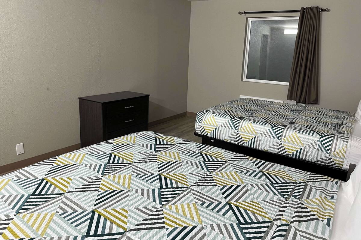 Ein Schlafzimmer mit zwei Betten, einem Schminktisch, einem Fenster mit Vorhängen und einer schlichten Wand.