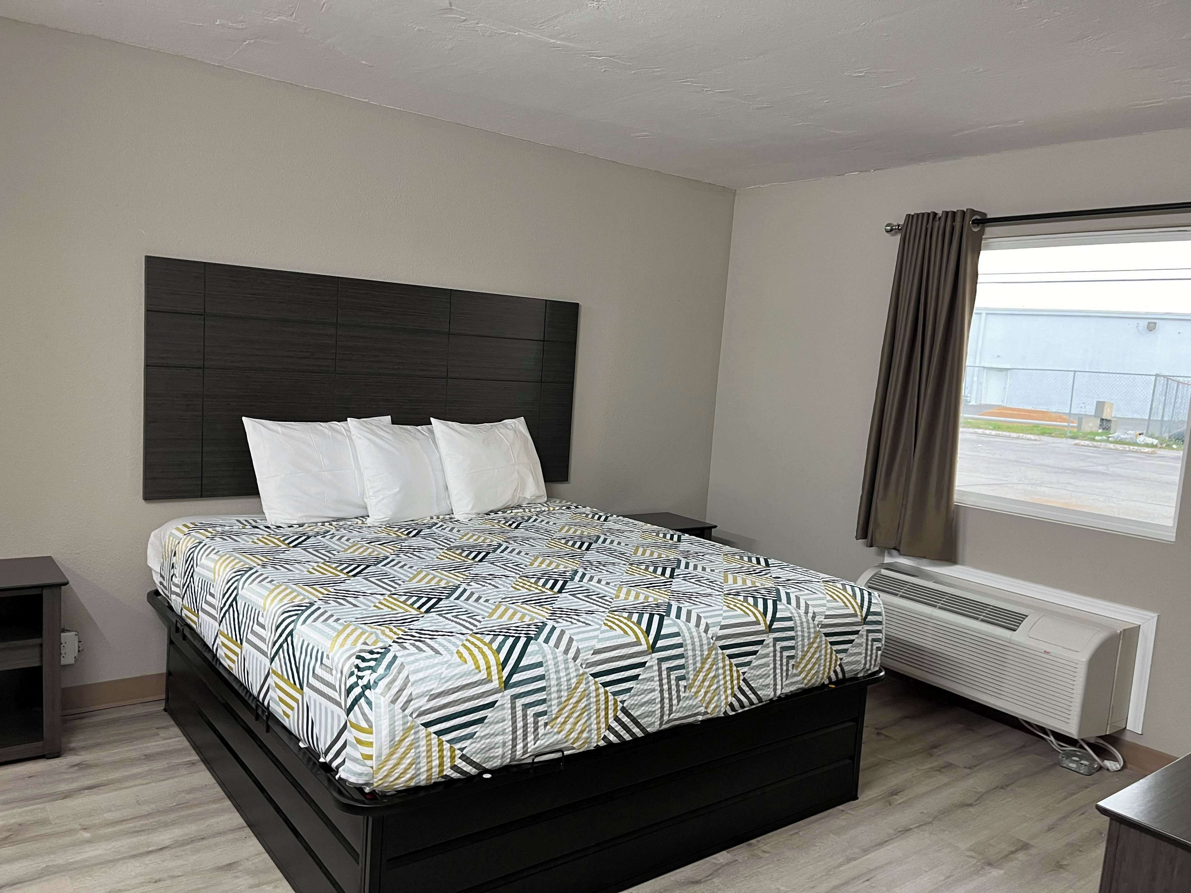 A bedroom with a bed, a headboard, a window with curtains, a heater, and a small table.