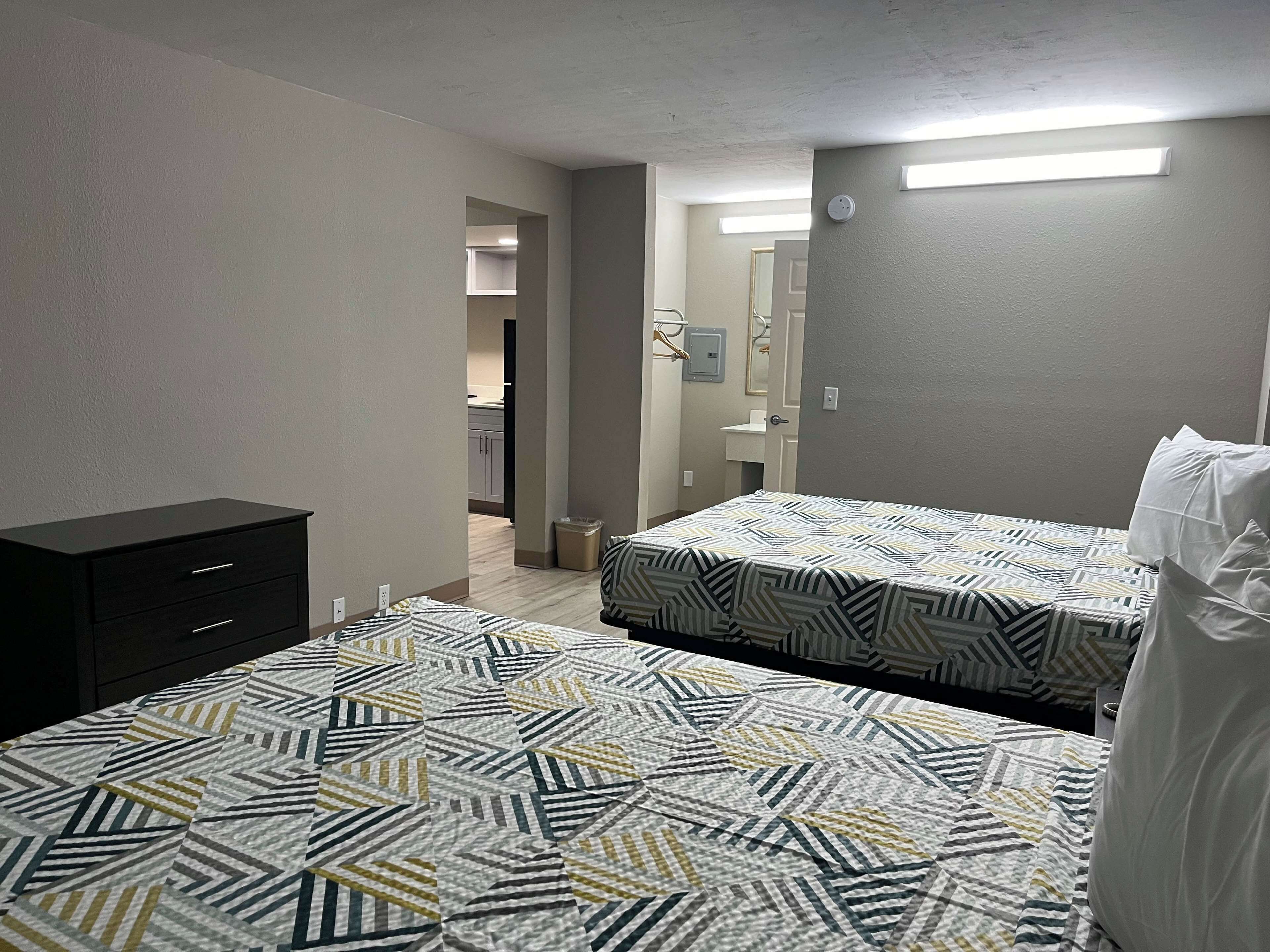 Un dormitorio con dos camas, un aparador y un baño visible a través de una puerta abierta.