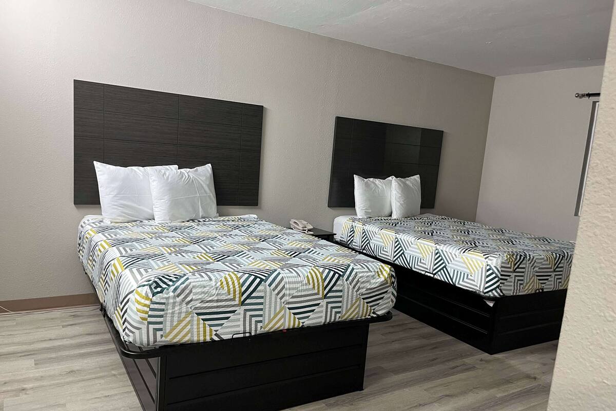 Ein Hotelzimmer mit zwei Betten, jeweils mit einem gemusterten Bettbezug und weißen Kissen, vor einer schlichten Wand mit einem dunklen Kopfteil.
