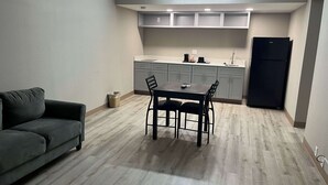A compact living space with a sofa, a dining table with chairs, a kitchen area with cabinets, and a refrigerator. - Studio 6 Suites West Memphis, AR - Memphis (West Memphis)