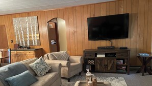 Una sala de estar con un sofá color beige, una mesa de centro, un televisor en la pared y paneles de madera.
