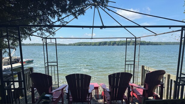 Una terraza de madera con sillas Adirondack y mesas de picnic con vista a un lago.