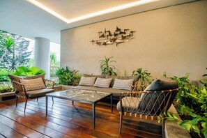 Relax in this stylish space with a sofa, armchairs, and a coffee table, surrounded by lush greenery and a unique art piece.