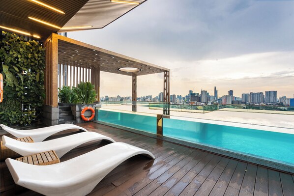 Enjoy breathtaking city views from our rooftop infinity pool, surrounded by comfortable lounge chairs and a glass railing.