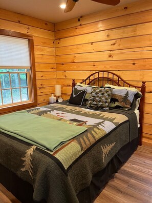 Quarto de cabana de madeira com cama, janela e ventilador de teto.