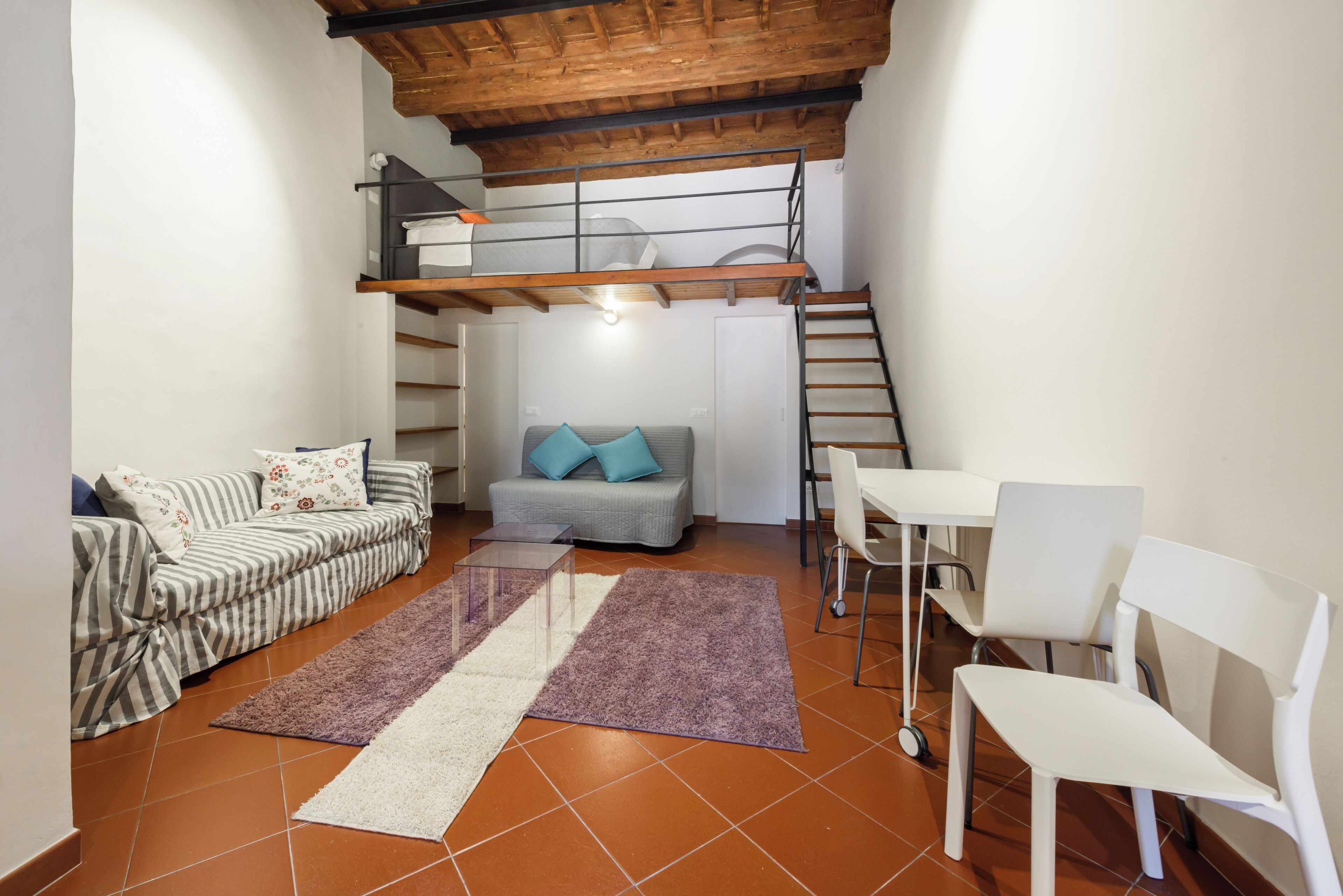 A compact living space with a sofa, a small table, a couch, a staircase, and a dining area.