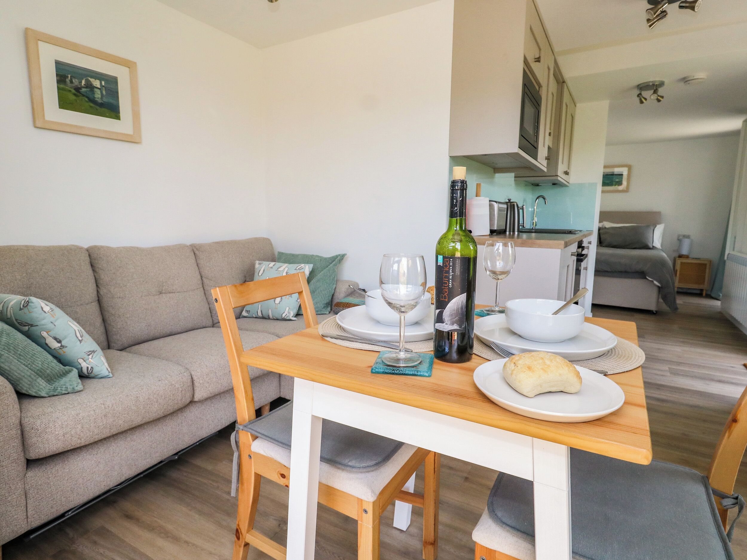 Een eetgedeelte met een houten tafel, stoelen, een fles wijn en een schaal brood.