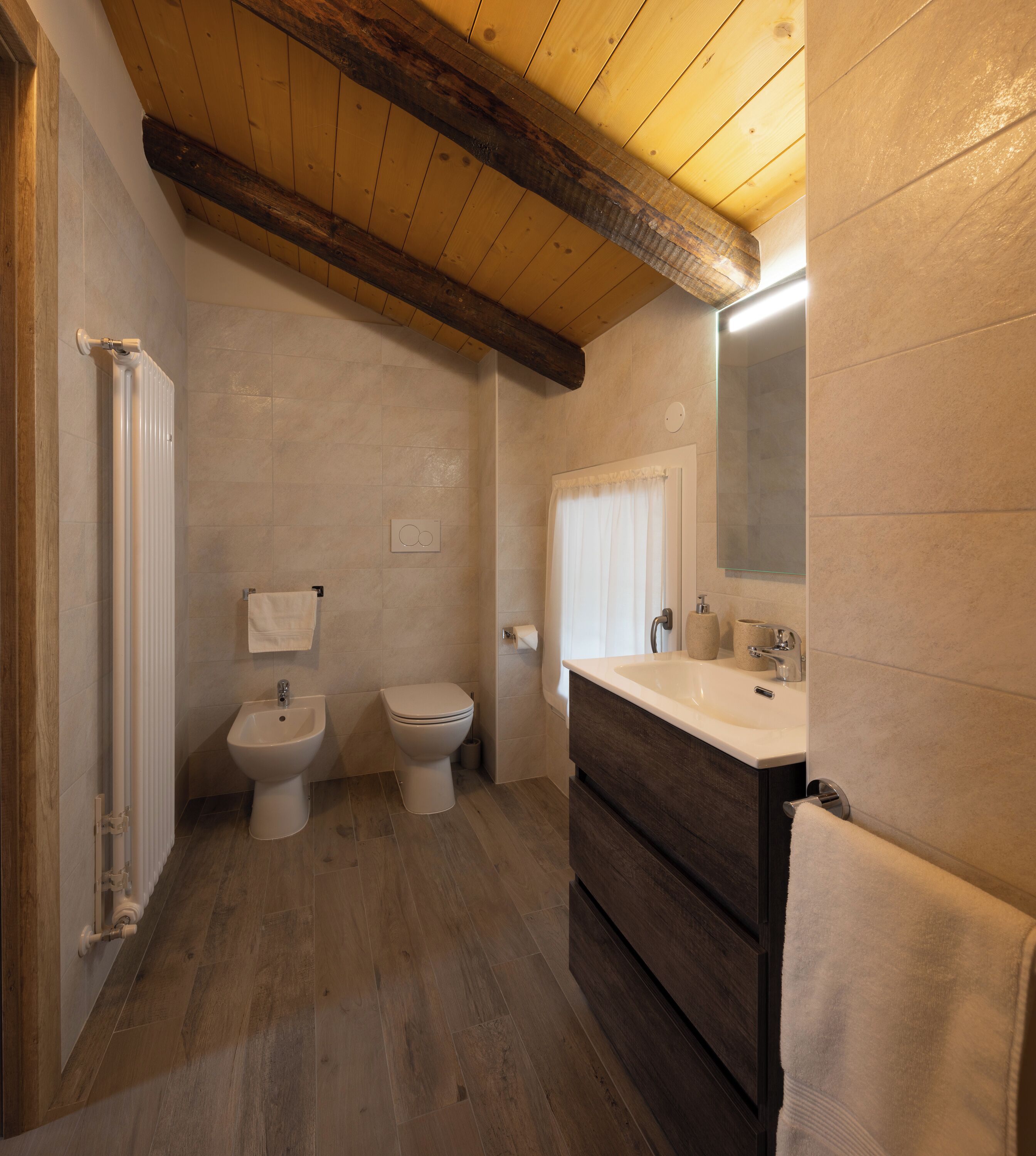 Un baño con techo de madera, un espejo grande, un lavamanos y dos inodoros.