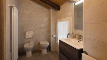 Un baño con techo de madera, un espejo grande, un lavamanos y dos inodoros.