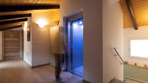 A hallway with wooden flooring, a staircase with a handrail, and a door with a light above it. - Vigna degli Angeli (Ragogna)