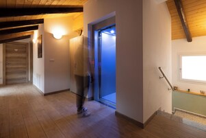 Un pasillo con suelo de madera, una escalera con barandilla y una puerta con luz encima.