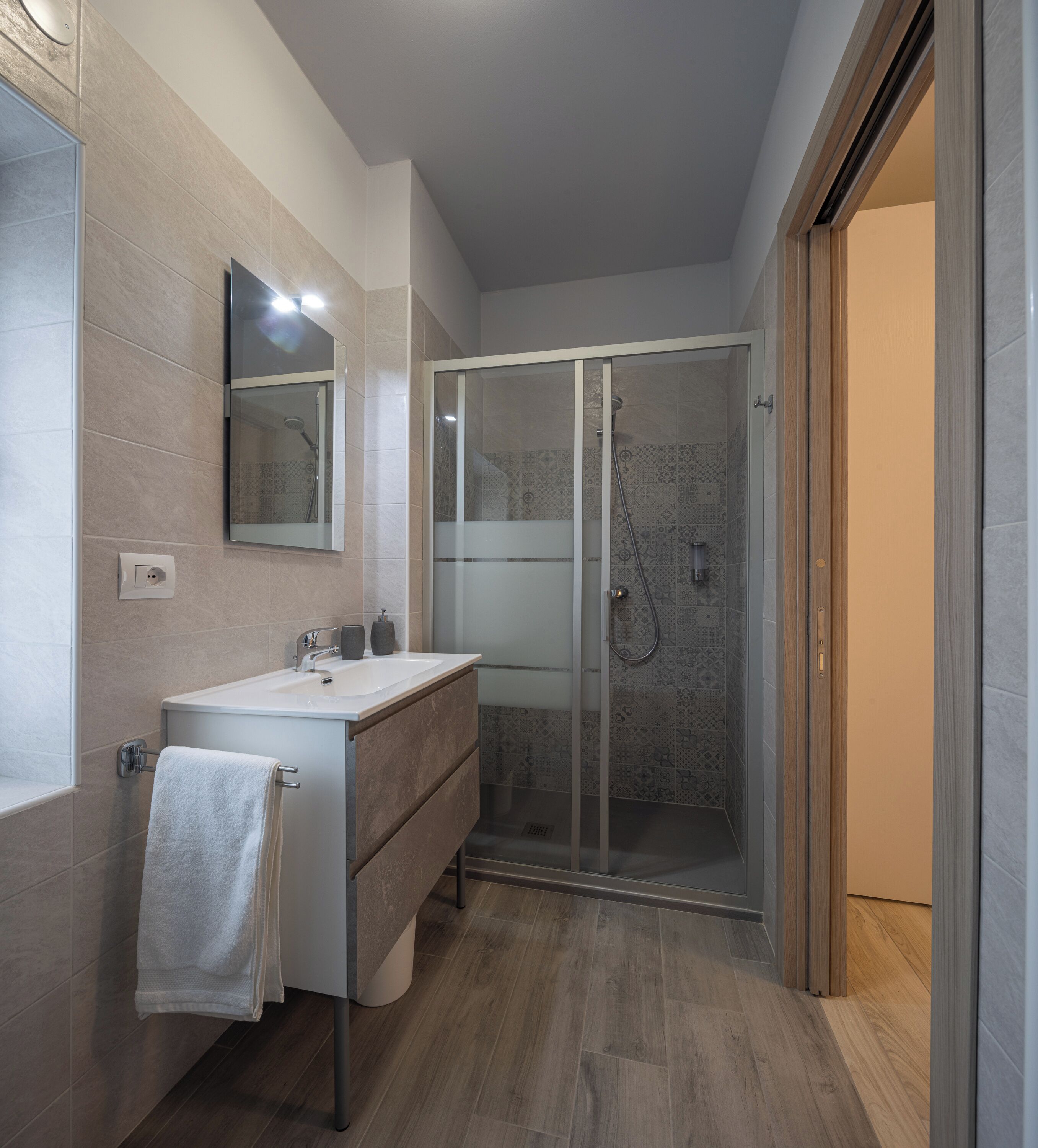 A modern bathroom with a glass-enclosed shower, a vanity with a mirror, and a towel hanging on a rack.