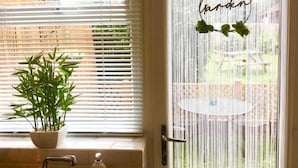 A room with a window featuring white blinds, a potted plant on the windowsill, and a door with a circular sign that reads "Garden". - Cosy Coach House Garden Apt by the Sea Res Parking (Broadstairs)