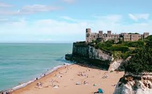 Une plage avec un château perché sur une falaise surplombant la mer.