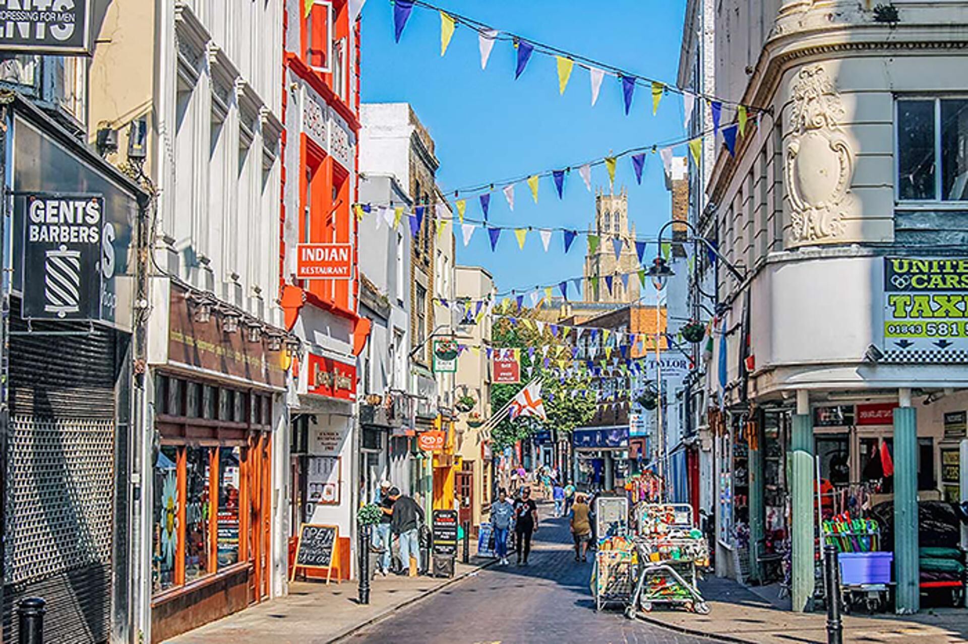 A street lined with shops, including a barber shop and a restaurant, under blue bunting.