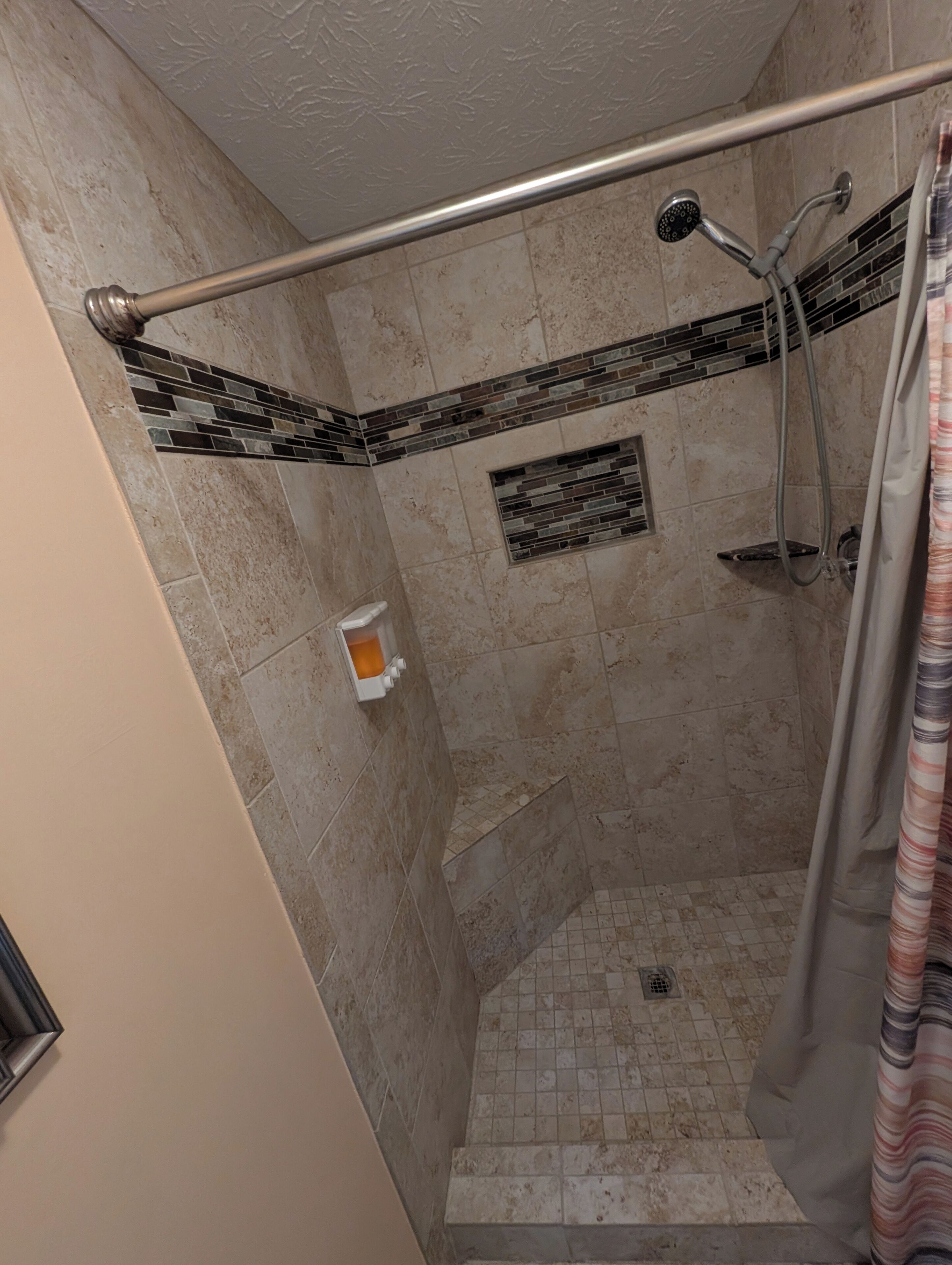 A shower with a metal grab bar, a tiled floor, and a small window with a brick pattern.