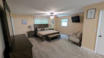 A bedroom with a bed, bedside tables, a chair, a dresser, a ceiling fan, and a TV mounted on the wall.