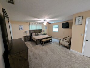 A bedroom with a bed, bedside tables, a chair, a dresser, a ceiling fan, and a TV mounted on the wall. - Cozy Elegant Cabin in the heart of Snellville forest (Snellville)