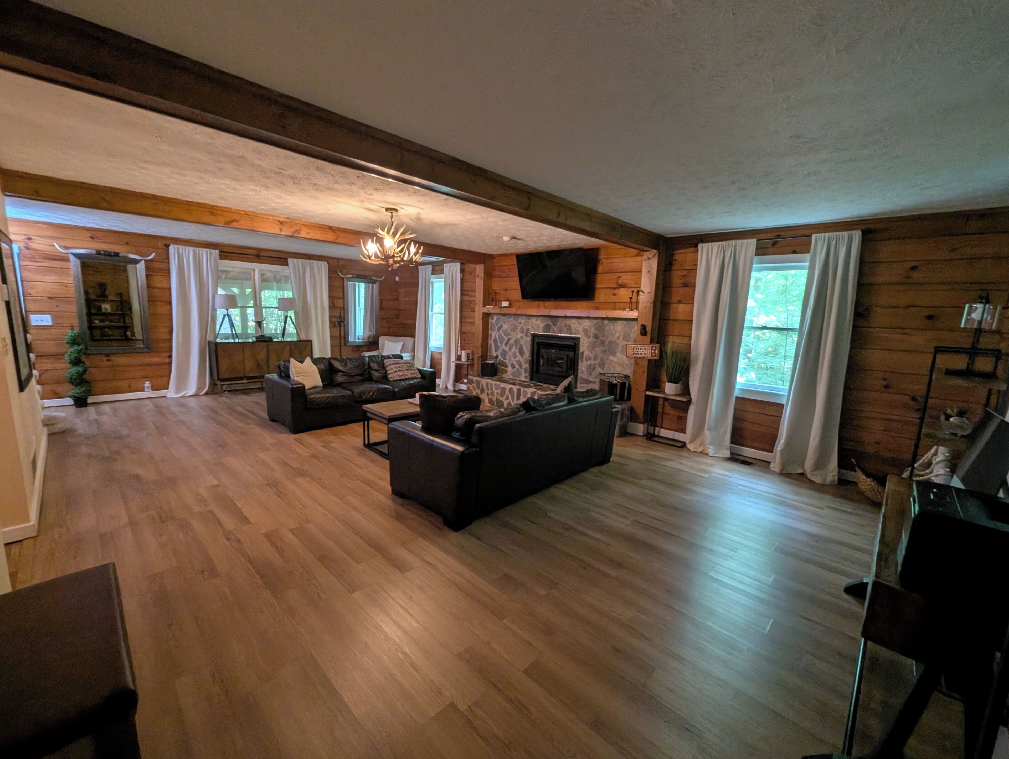 A spacious living room with a fireplace, wooden floors, and a television mounted on the wall.
