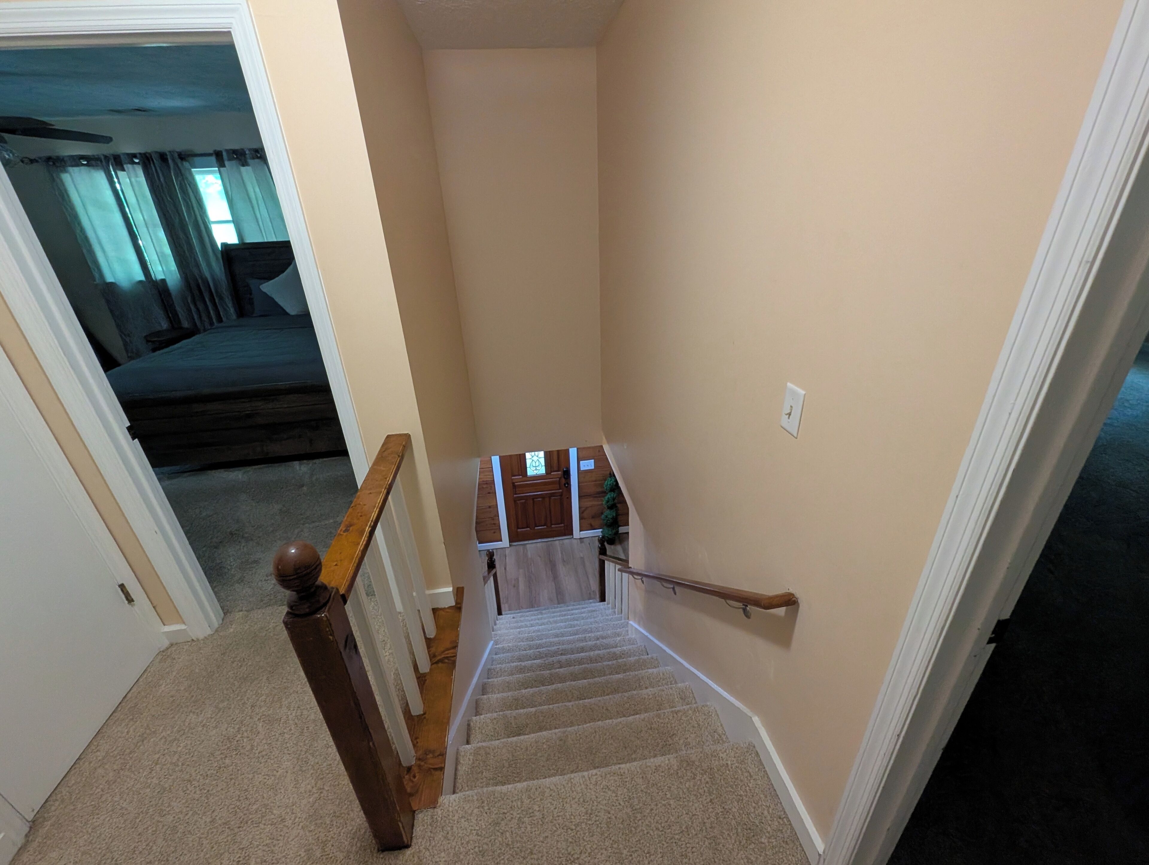 Un escalier recouvert de moquette, doté d’une rampe en bois, menant à un palier avec une porte et une petite fenêtre.