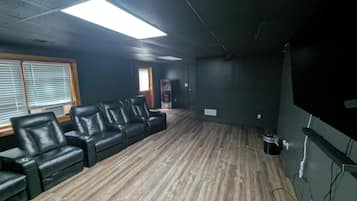 A room with a wooden floor, black leather seating, a large screen, and a door in the background.