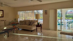 A living room with a sofa, coffee table, and a ceiling fan. There is a sliding glass door leading to an outdoor area with a pool. - Ferienvilla Bell Villa Bonita Springs (Bonita Springs)